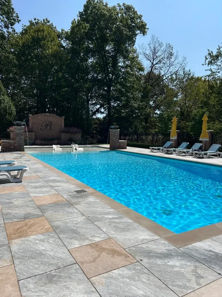 Luxury swimming pool with lounge chairs, yellow umbrellas, brick wall, and surrounding trees