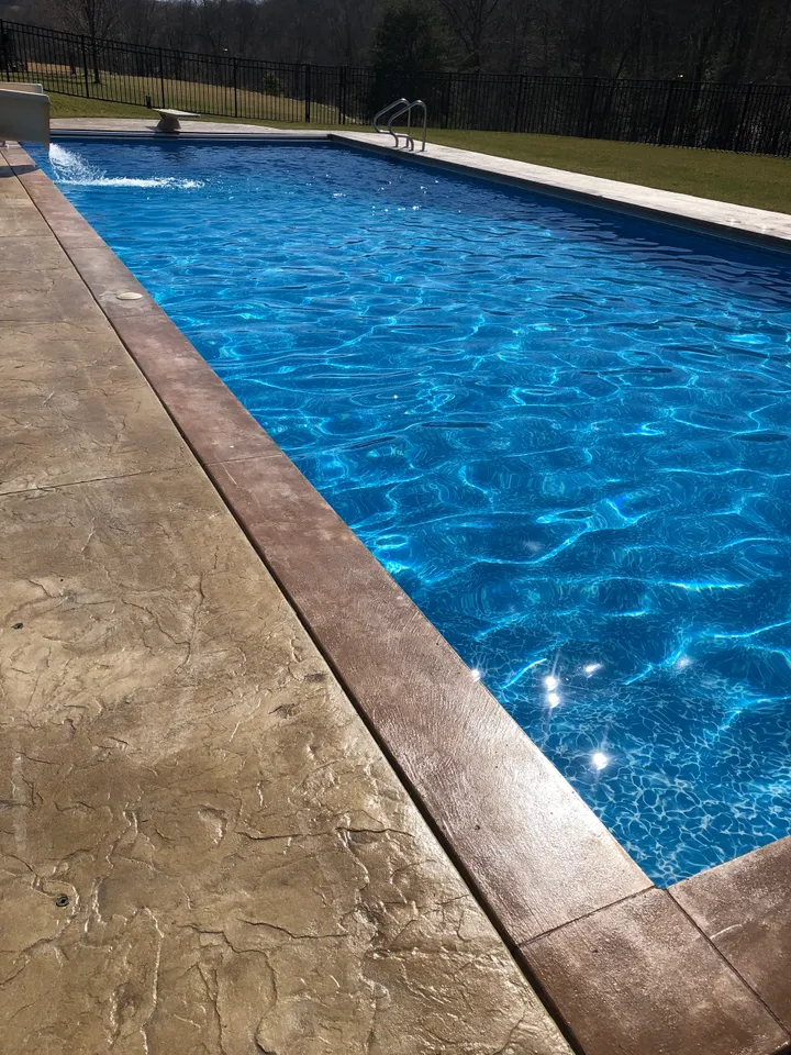 Clear blue swimming pool with water feature and textured concrete deck