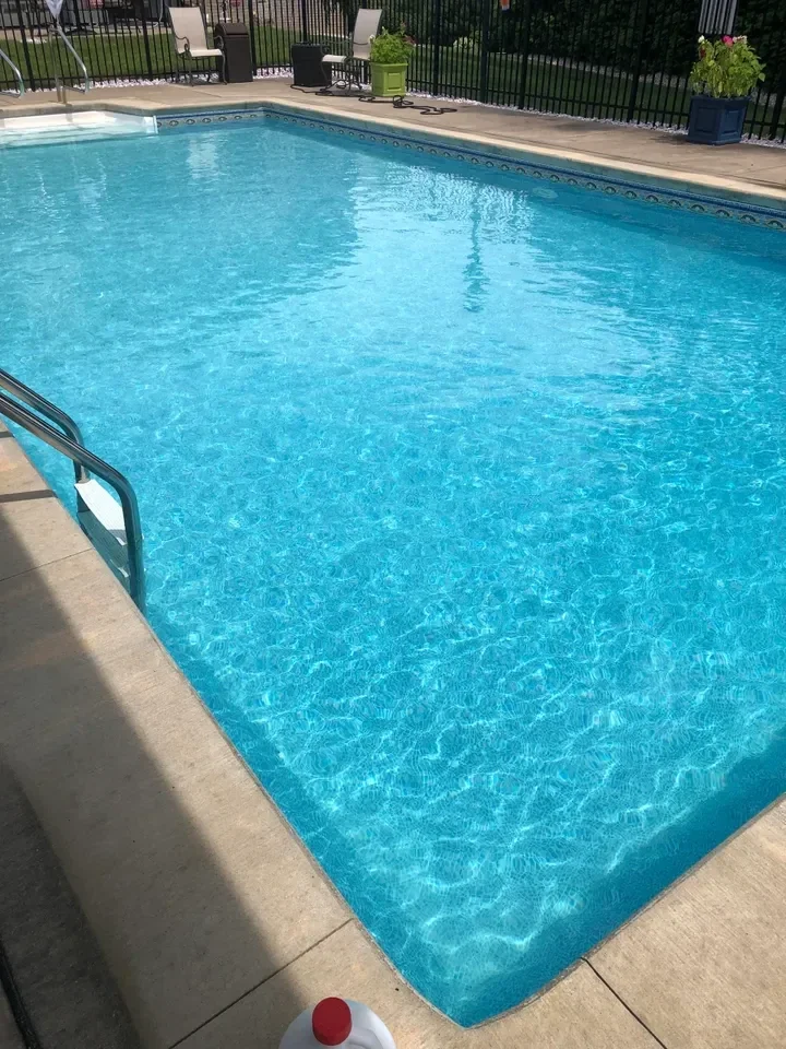 Rectangular swimming pool with clear turquoise water and concrete deck surrounded by black fence.