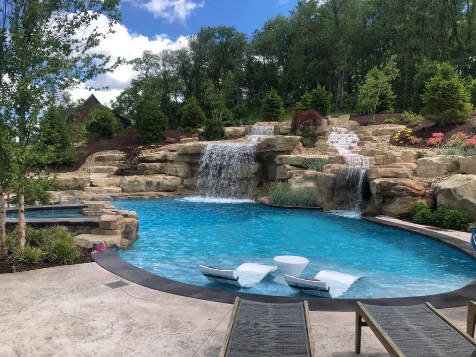 Luxury backyard pool with turquoise water, cascading waterfall, stone features, and lounge chairs