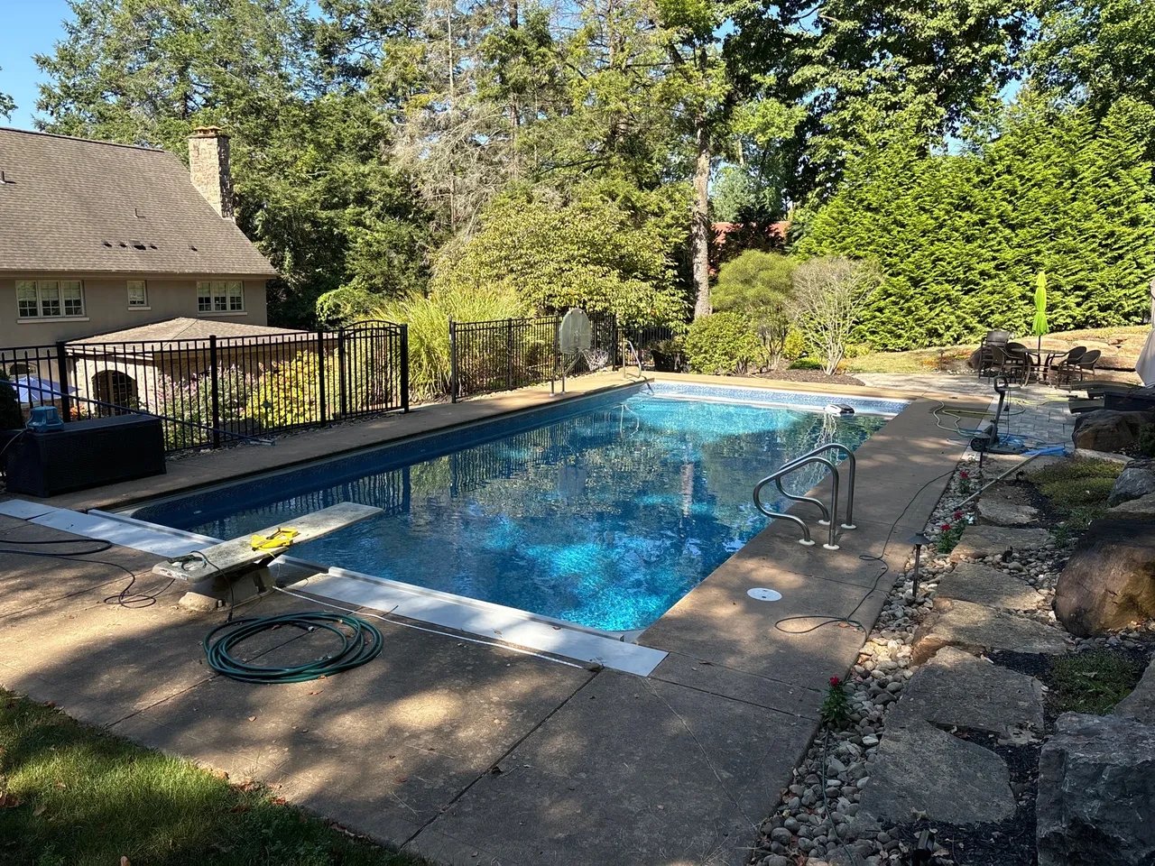 Backyard swimming pool with blue water surrounded by stone patio and trees