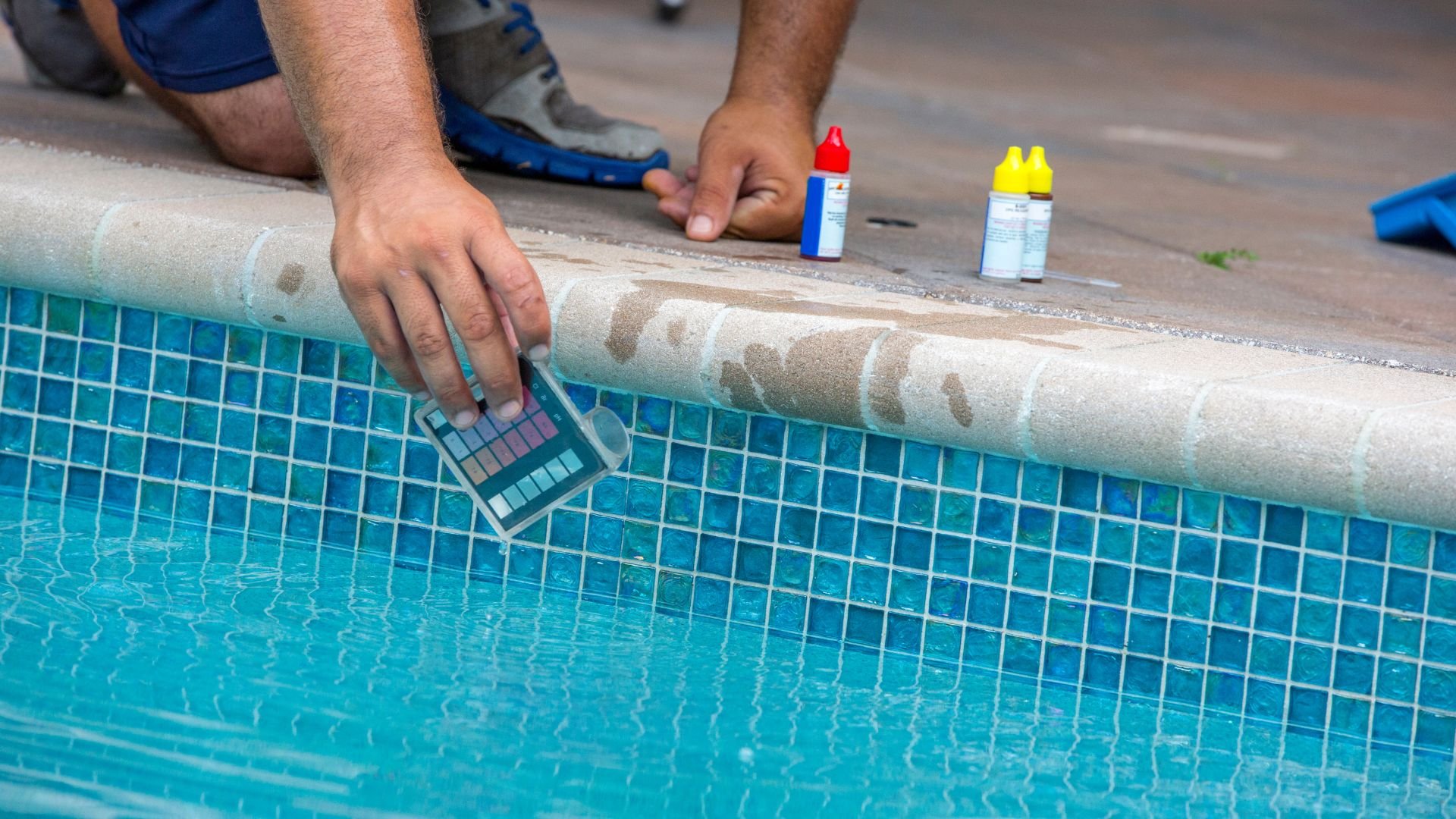 Checking pool water chemistry with test kit and chemical bottles nearby