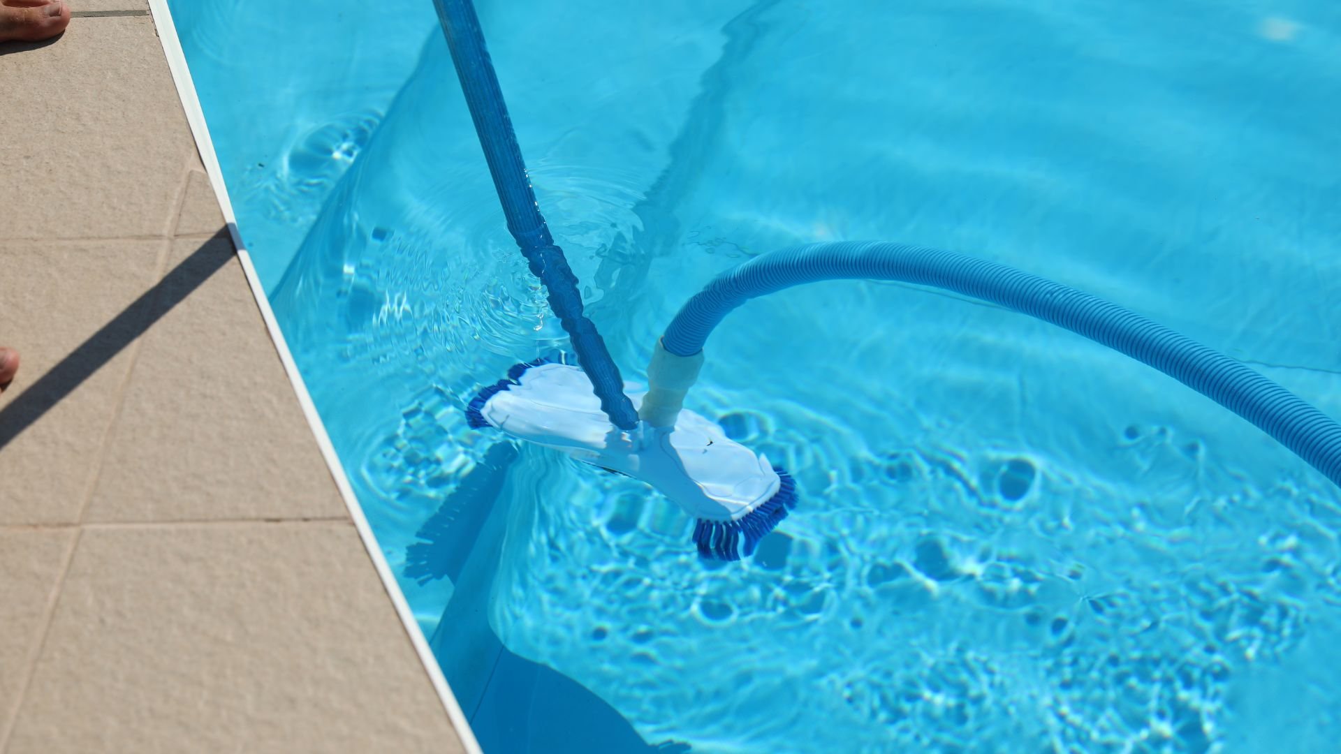Pool cleaning tool vacuuming blue water near pool edge