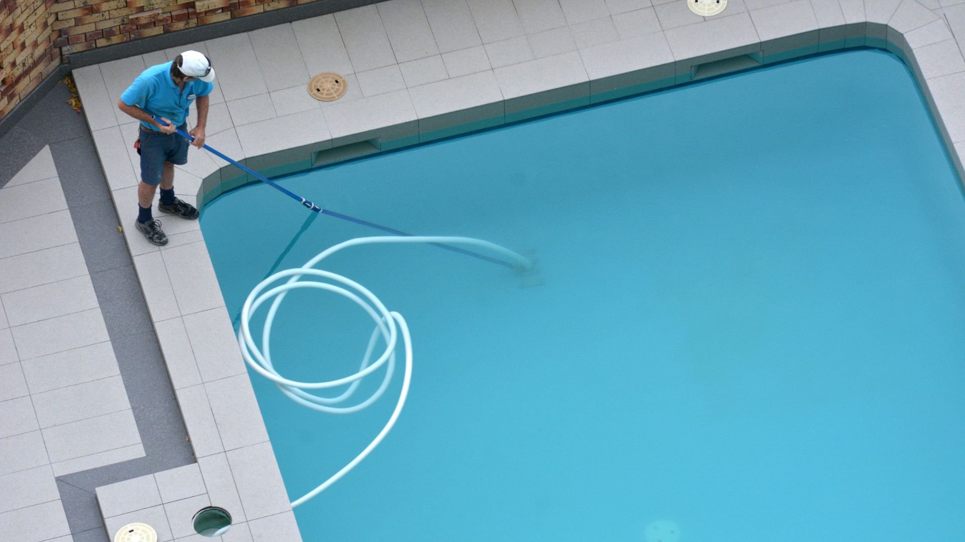 Pool maintenance worker cleaning swimming pool with blue vacuum hose