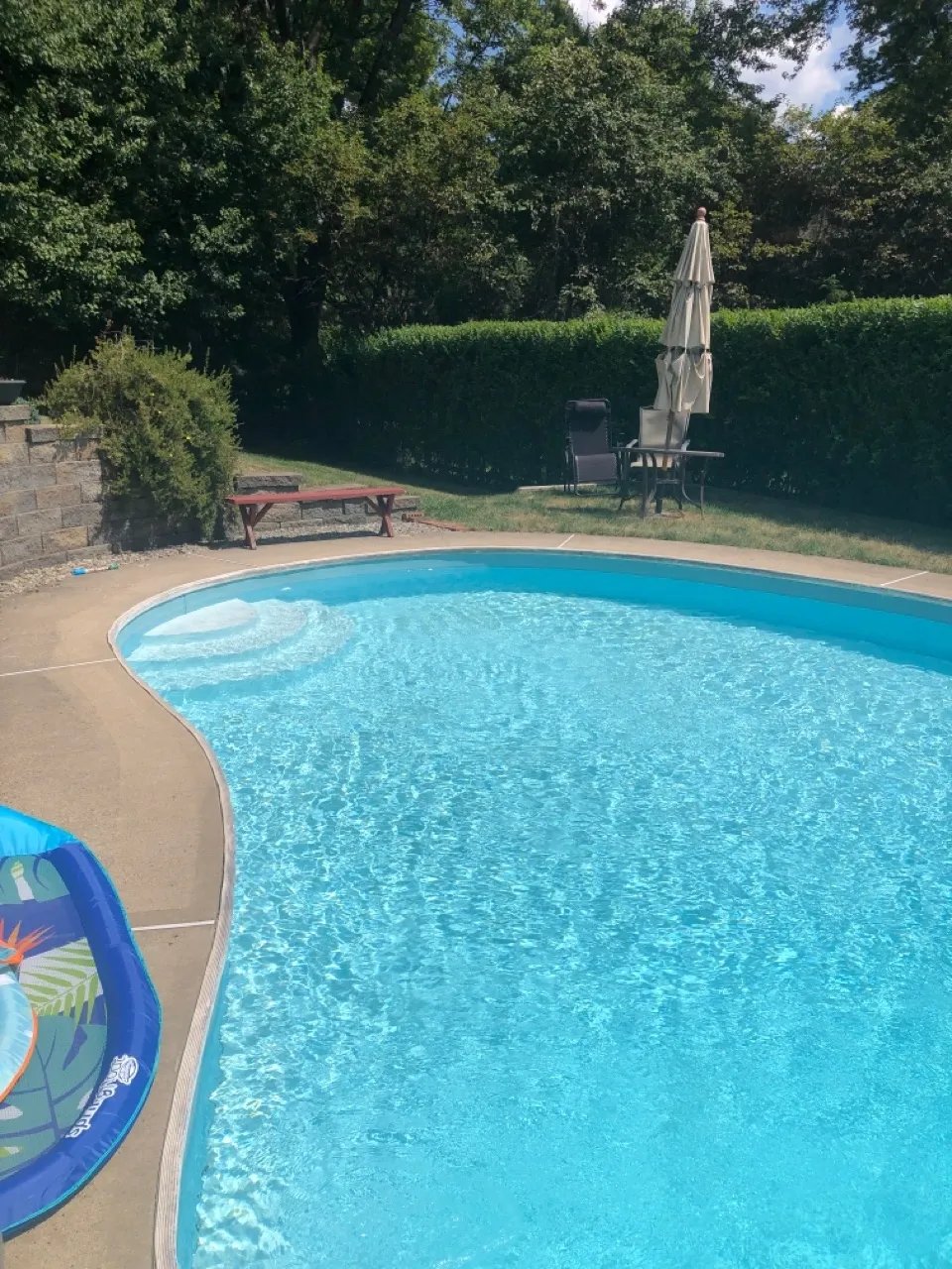 Backyard swimming pool with clear blue water, umbrella, and seating area