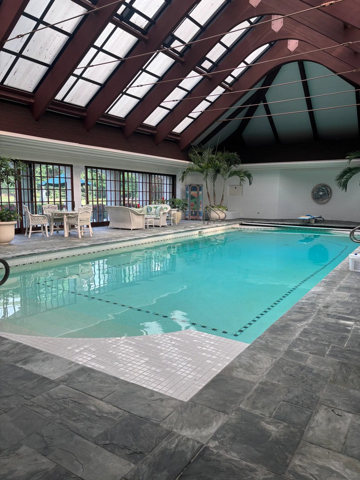 Indoor swimming pool with skylights, stone floor, and wicker furniture