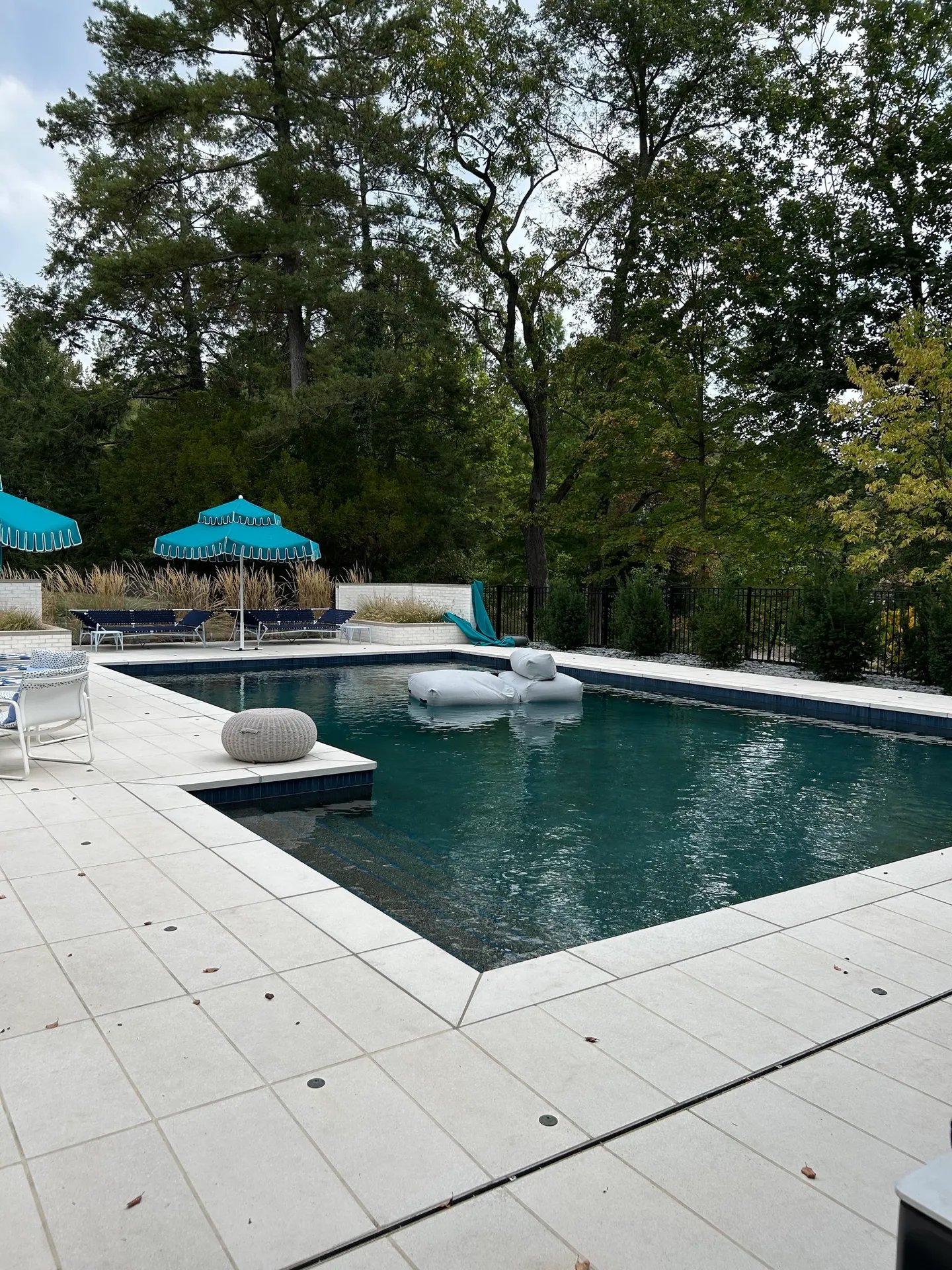 Backyard swimming pool with teal umbrellas and white lounge chairs