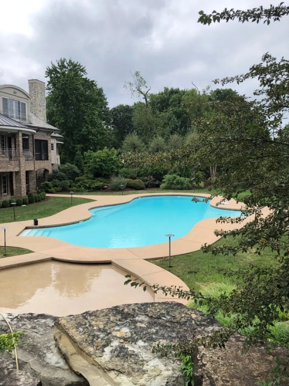 Luxury brick house with blue swimming pool surrounded by lush landscaping